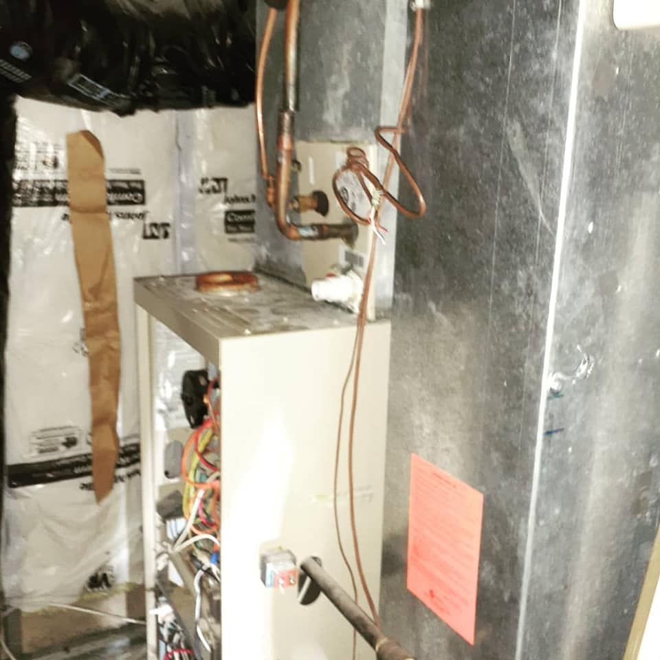 HVAC unit with exposed wiring, copper pipes, and metal ductwork in a basement setting.