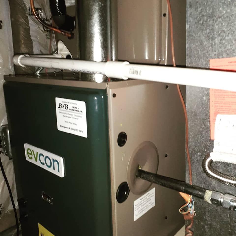 Green and gray furnace with connected pipes and labels, in a basement setting.
