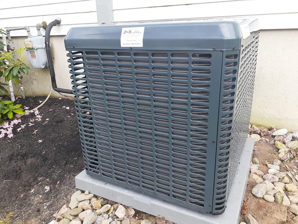 Gray air conditioner unit outside a building, set on a concrete pad with surrounding rocks.