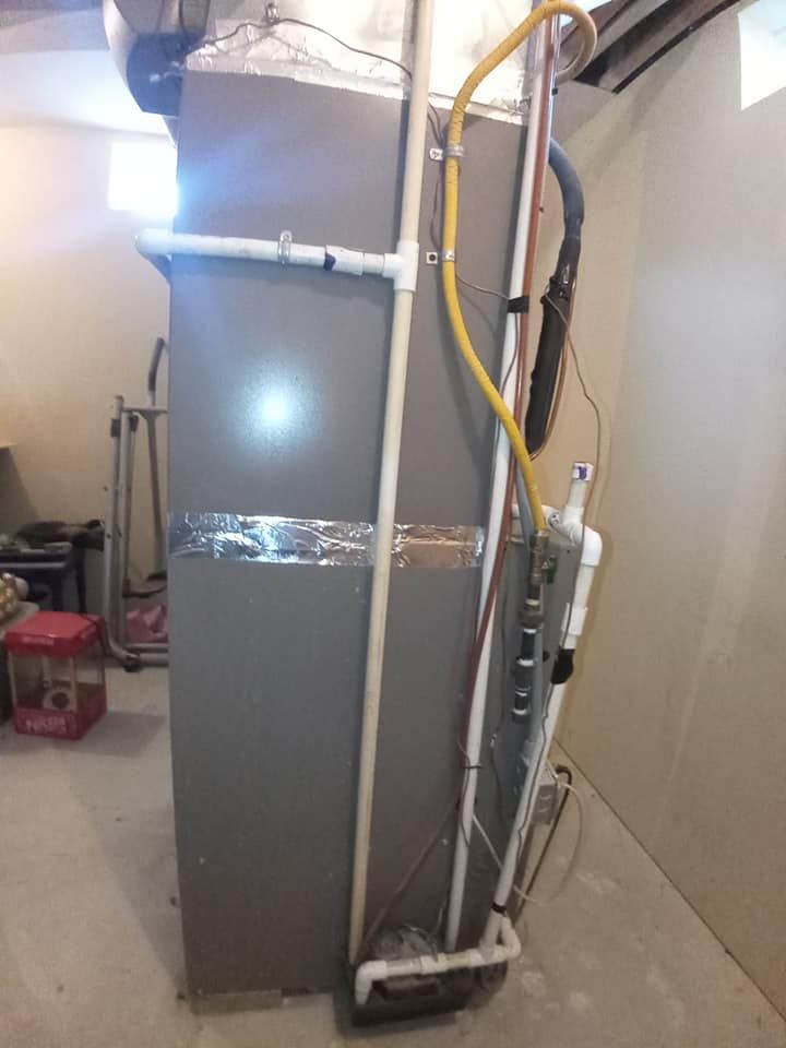 A tall, gray furnace in a basement setting with various pipes attached.