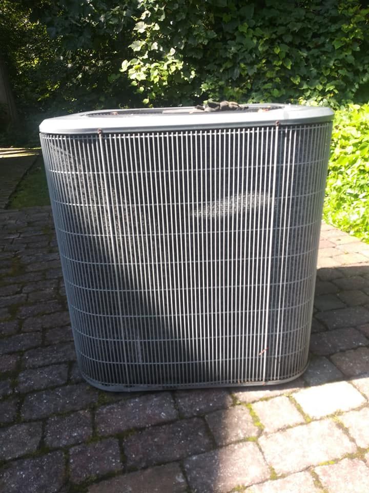 Air conditioning unit, outdoor setting, brick patio, surrounded by greenery.