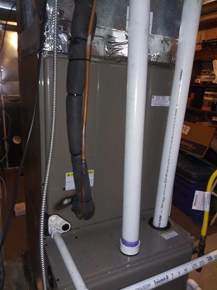 HVAC system in a utility room. Gray furnace with white PVC pipes and insulated black tubing.