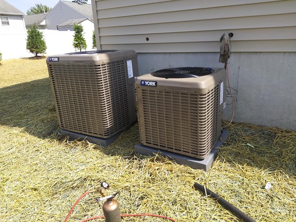Two brown YORK air conditioning units on concrete pads next to a beige house.