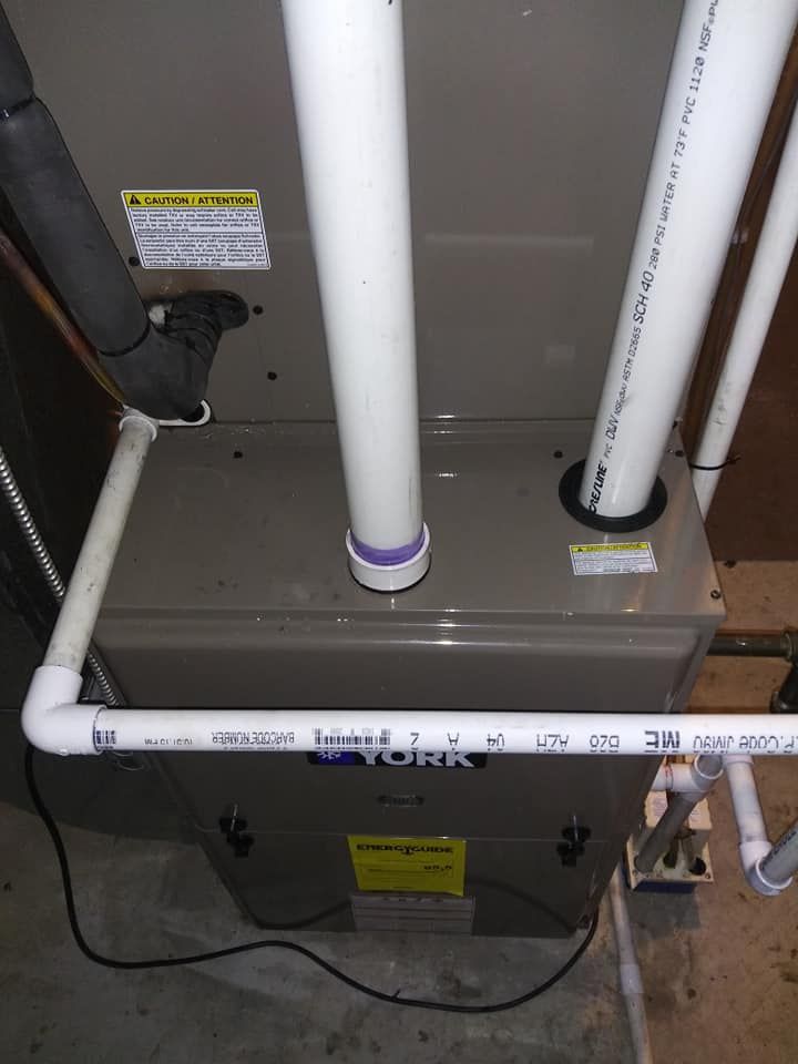 A gray York furnace with white PVC pipes for exhaust and intake in a basement setting.