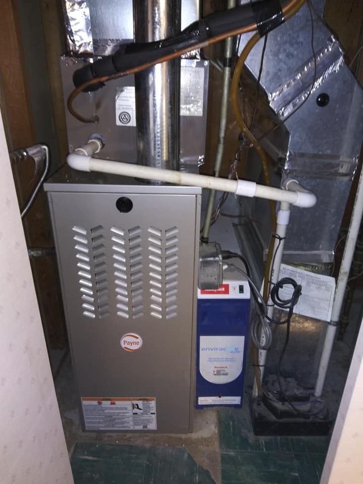 A gas furnace in a closet with ductwork and a humidifier. Gray furnace, white PVC pipes.
