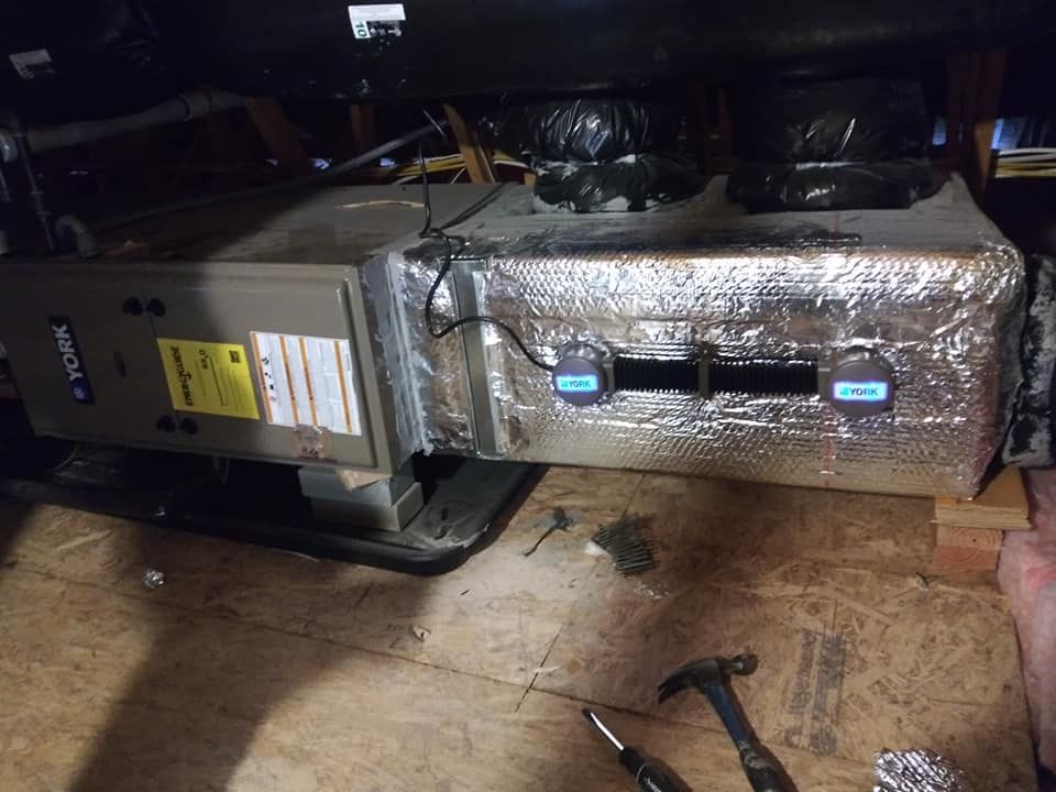 An HVAC system in an attic. It is partially covered in silver insulation.
