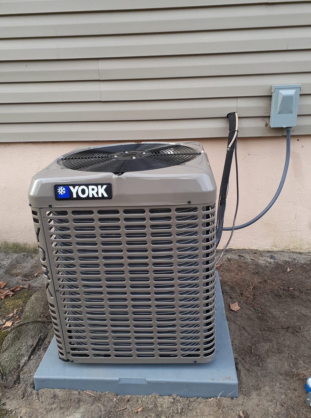 A York air conditioning unit is outside on a concrete pad near a wall with gray siding.