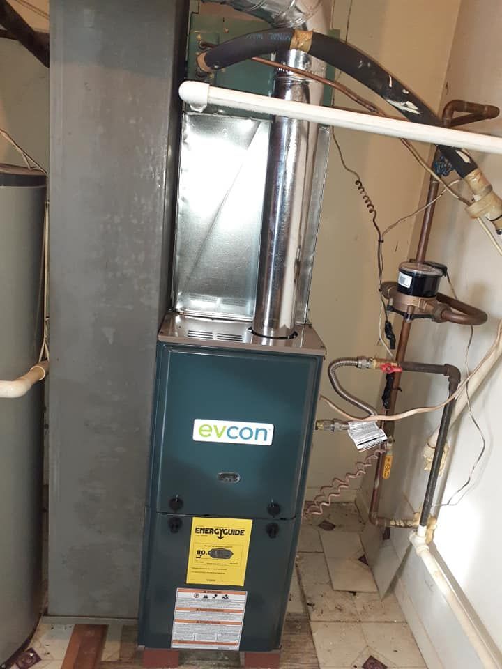 An Evcon furnace in a utility room, with attached metal ductwork and pipes, near a water heater.