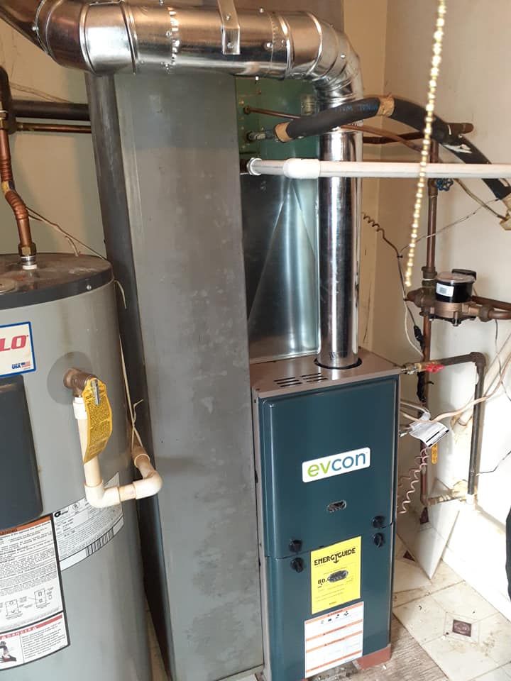 A furnace and water heater in a utility room. The furnace is blue with silver pipes. The water heater is gray.