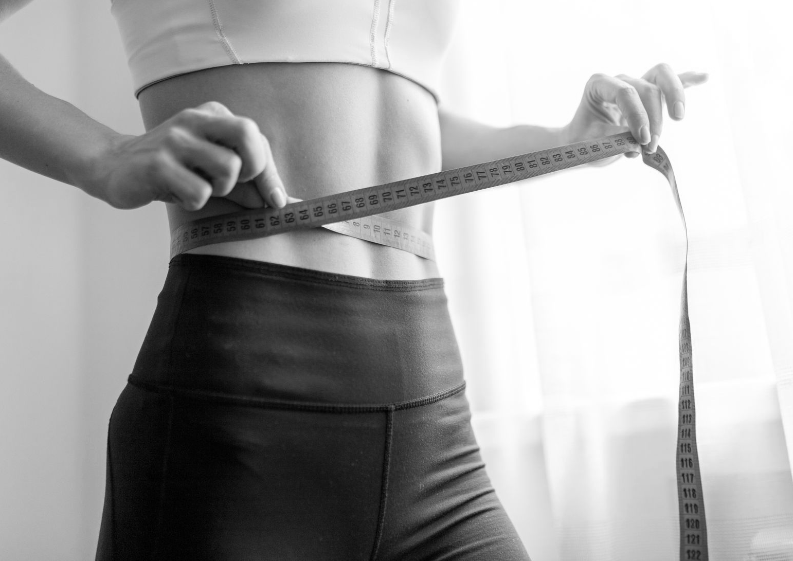 Person measuring waist with a tape measure; fitness focused.