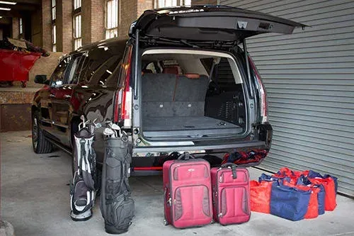 The trunk of a car is open and filled with luggage and golf clubs.