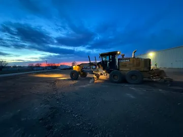 A bulldozer is sitting in a parking lot at night.