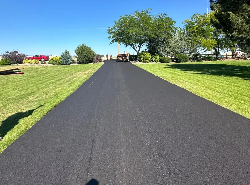 A black asphalt driveway going through a lush green field.