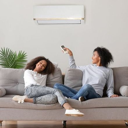 Two women are sitting on a couch holding remote controls.