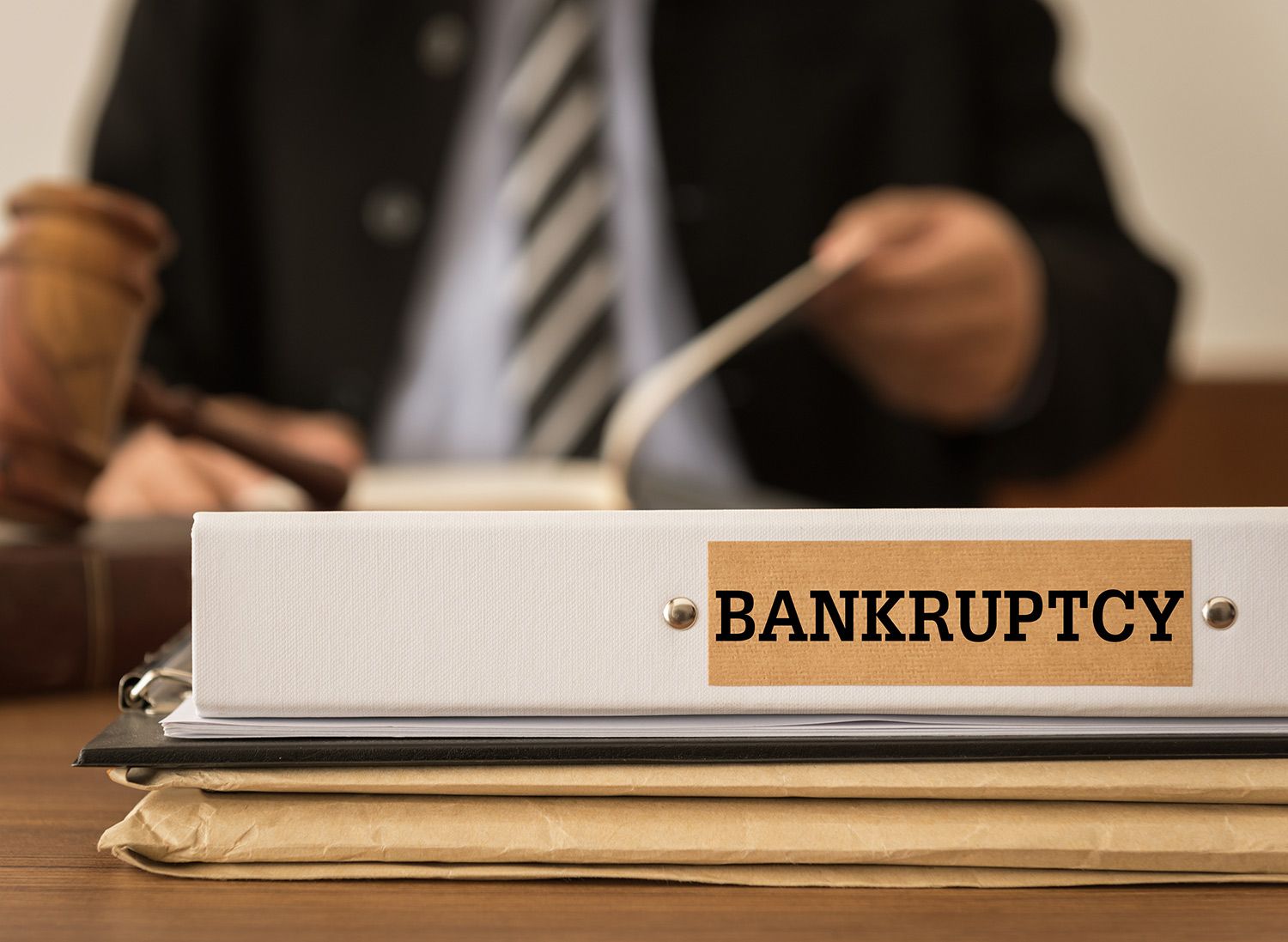 Bankruptcy binder with gavel and suited figure at desk.