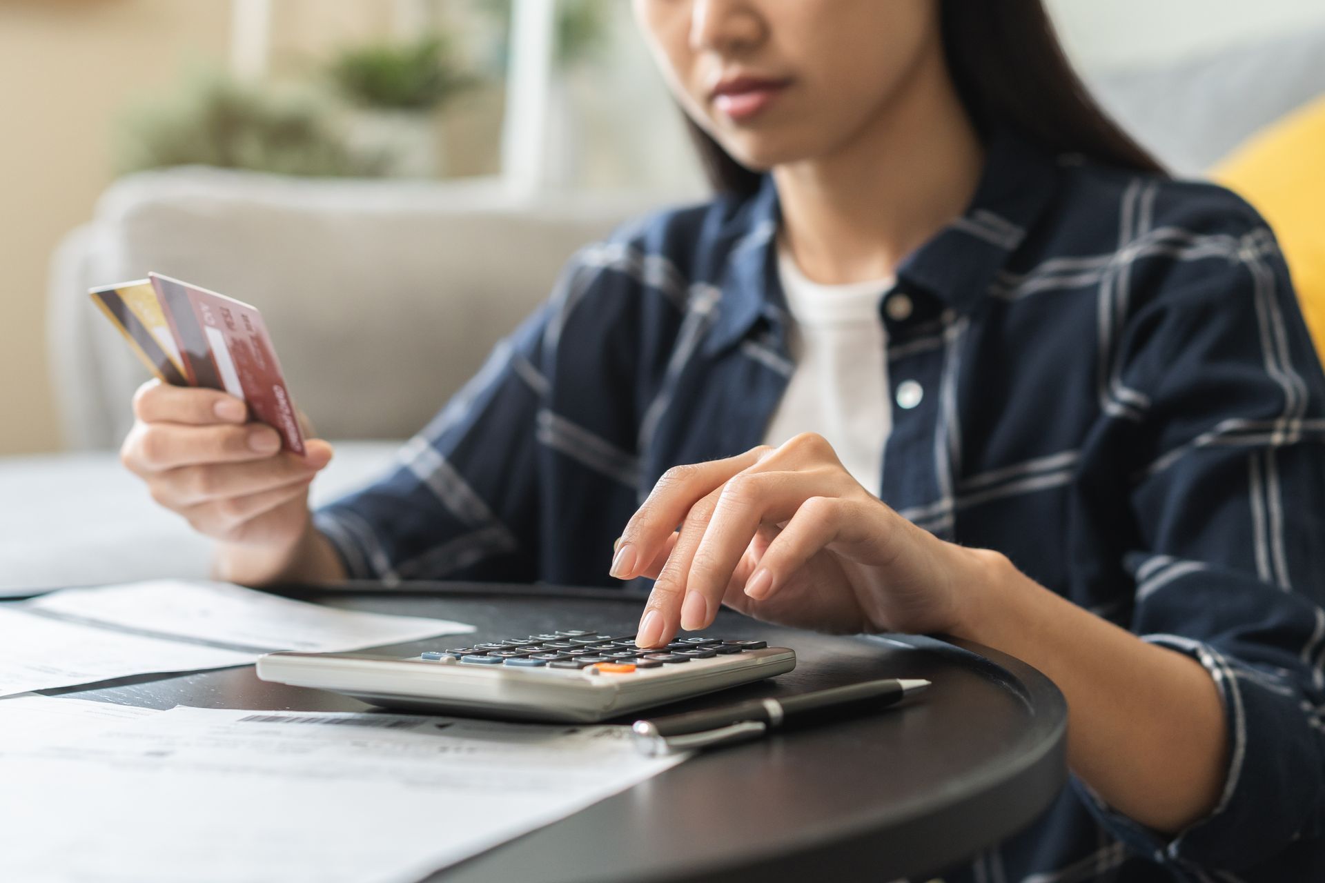 A stressed young woman holding two credit cards and using a calculator to calculate her expenses.
