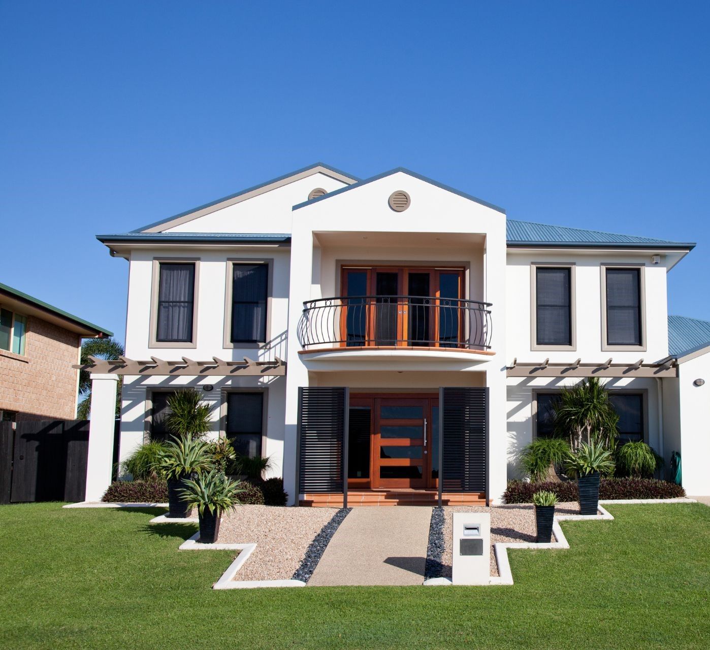 Two-story white house with blue roof; lawn, walkway, and landscaping; sunny day.