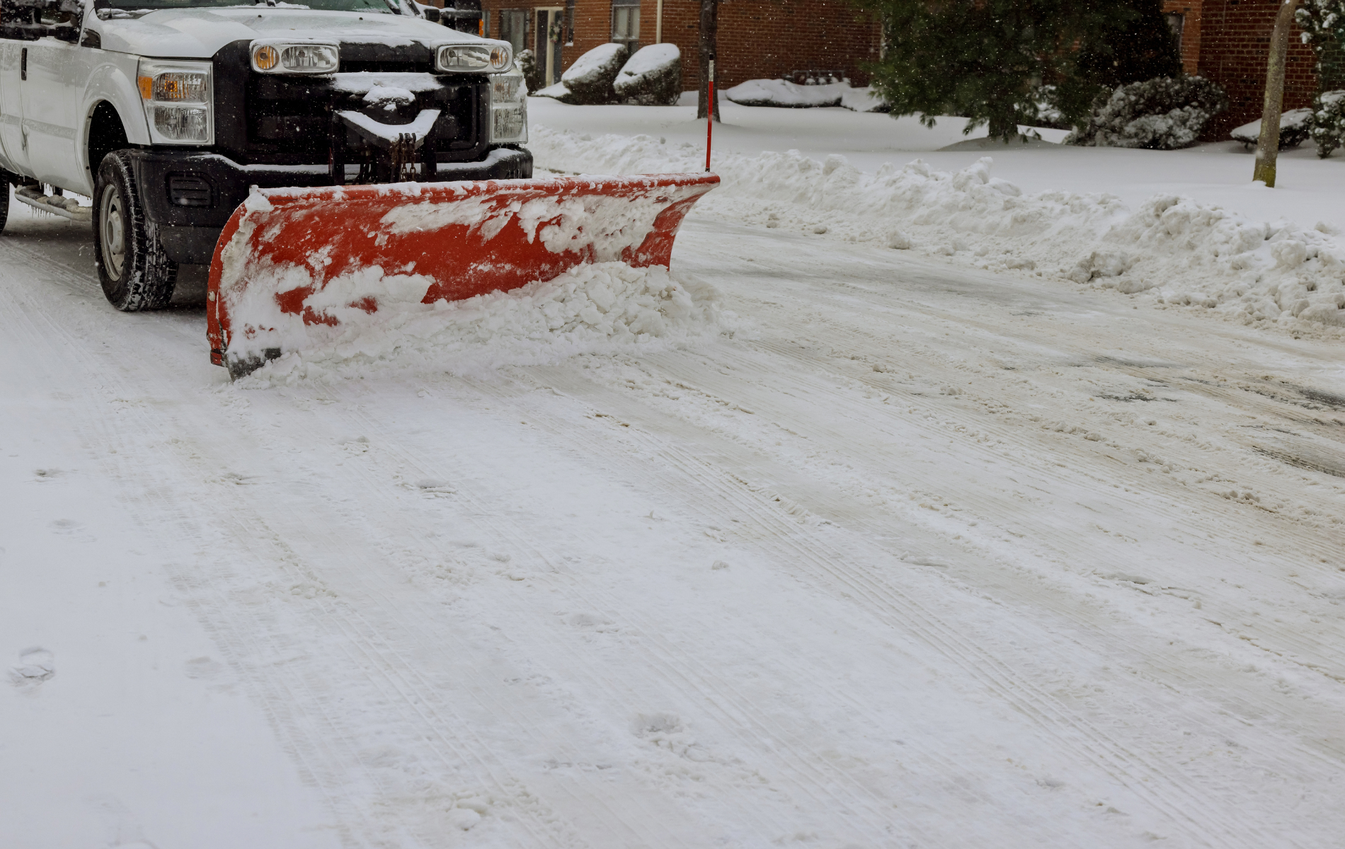 A white truck is plowing snow on a snowy street.