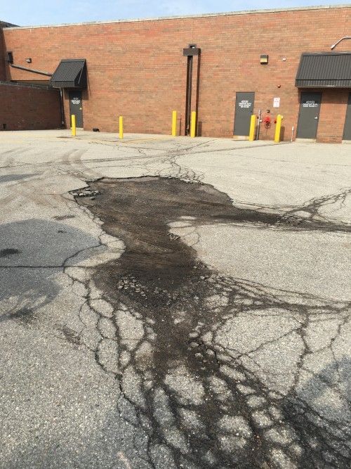 A cracked asphalt road in front of a brick building