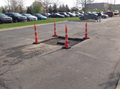 A parking lot with a hole in the ground and orange cones