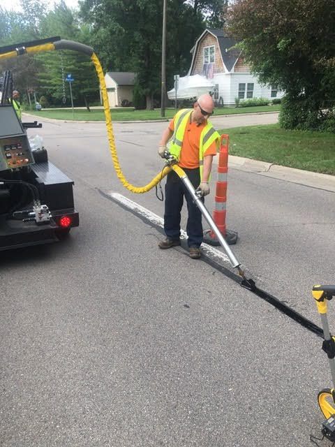 A man is standing on the side of the road holding a hose.