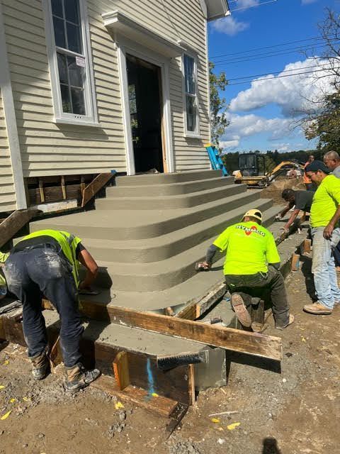 A group of construction workers are working on concrete steps in front of a house.