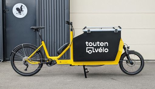 Un vélo cargo jaune est garé devant une porte de garage.