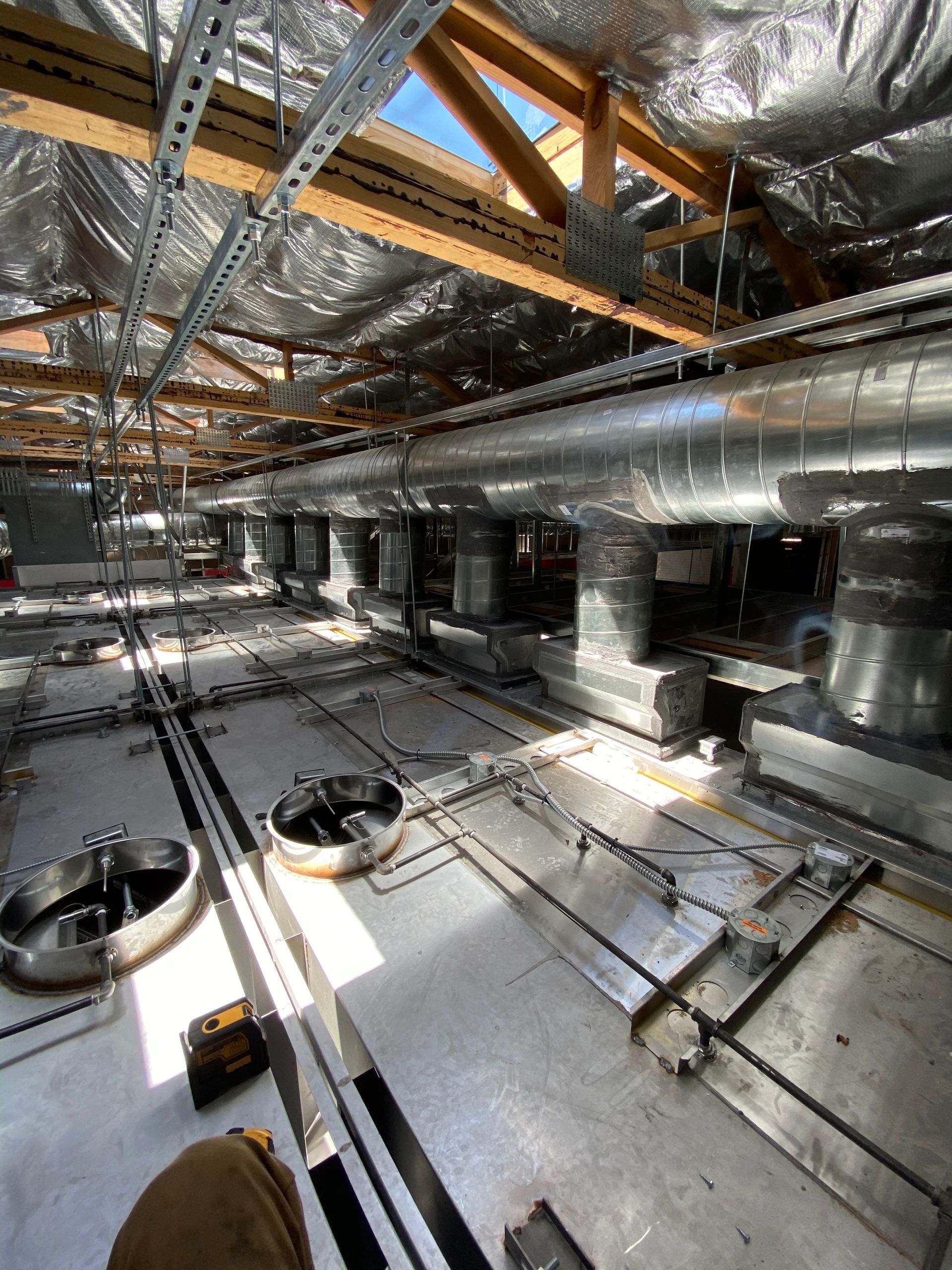 Interior view of a construction site with silver ductwork, metal framework, and unfinished flooring.