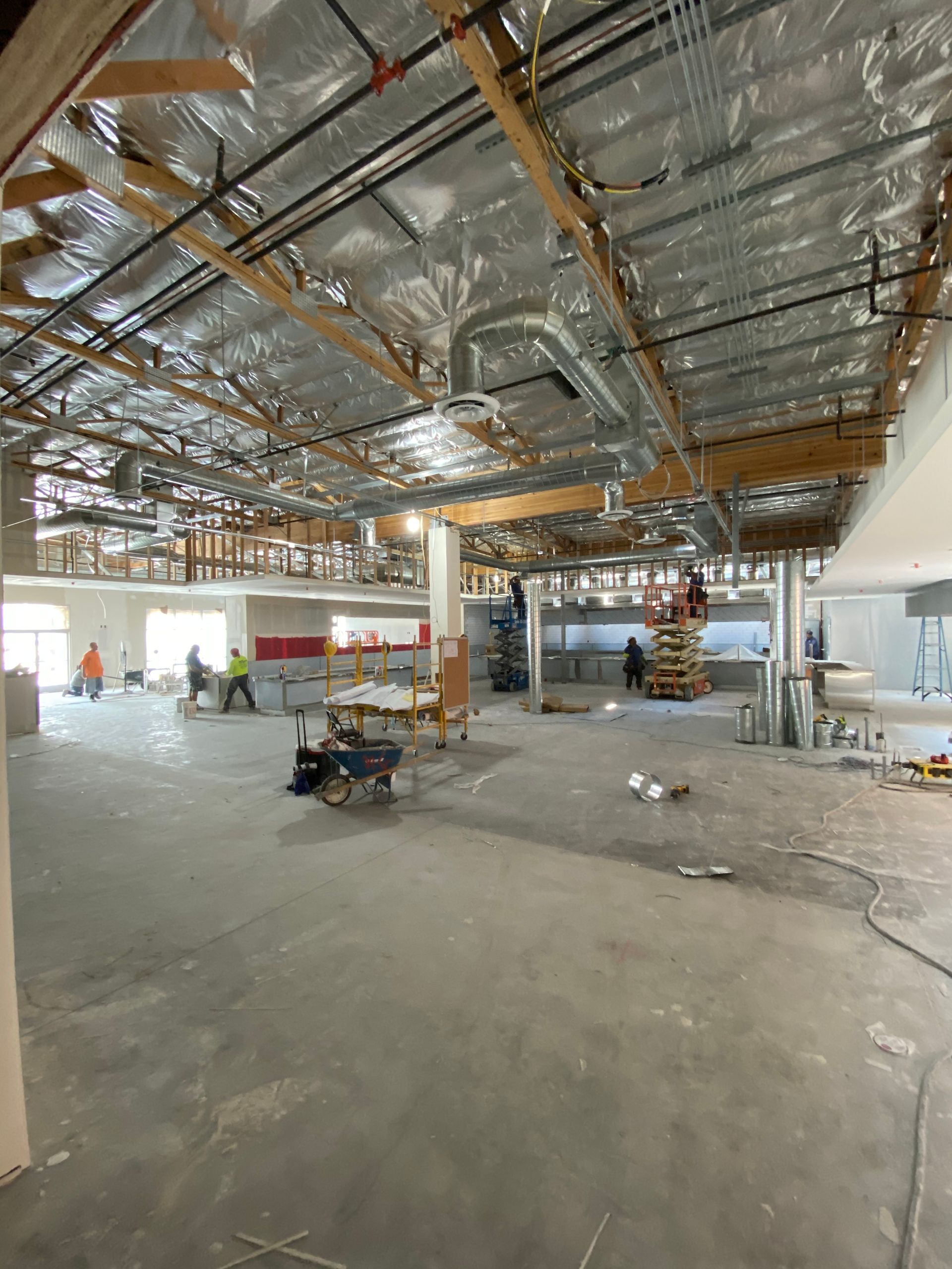 Construction site: open space with exposed ceiling, workers, and concrete floor.
