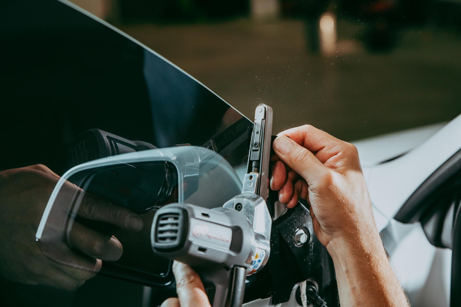 Person using a heat gun and tool to apply tint film on a car window.
