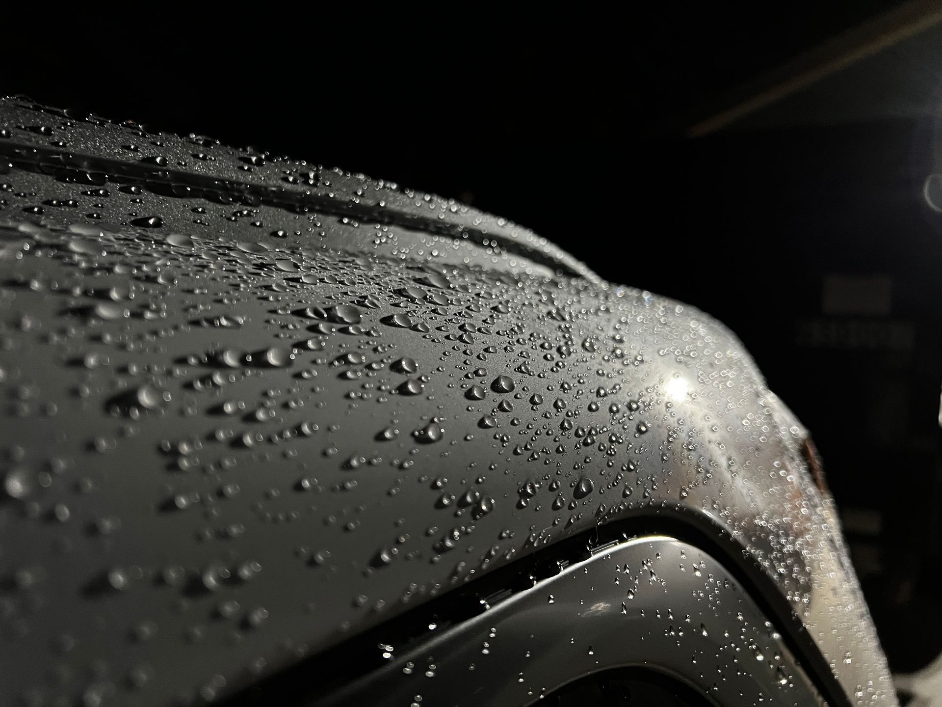 A gloved hand applies coating to a car's surface with a foam applicator in a well-lit workshop.