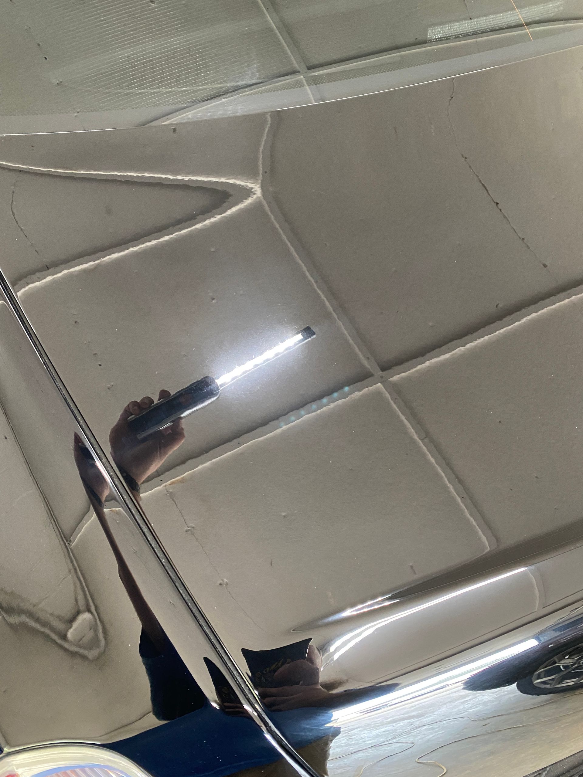 Person holding a flashlight, examining the shiny surface of a vehicle, reflecting light.