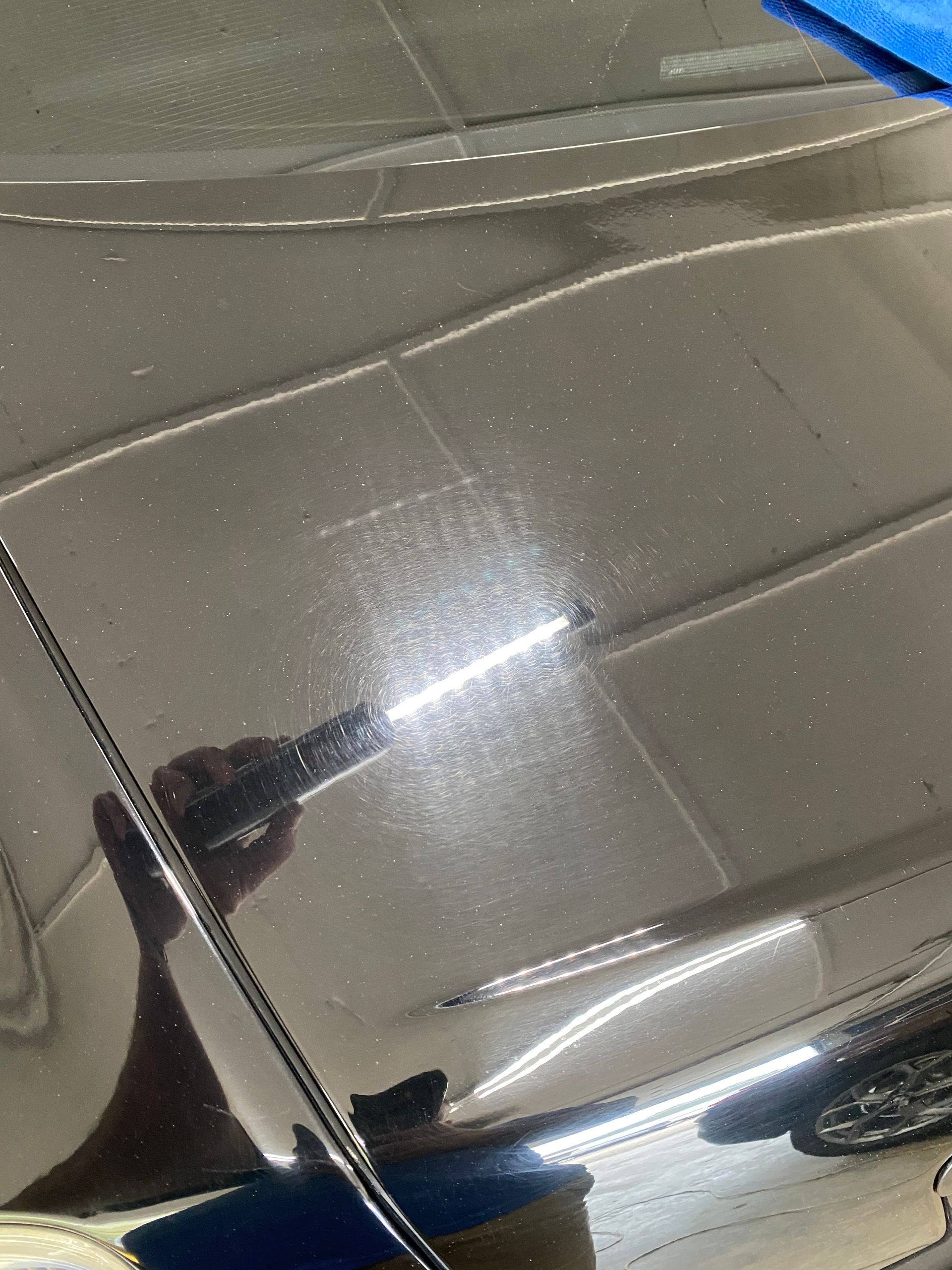 Black car hood with light reflections and scratches. A hand holding a tool is visible.