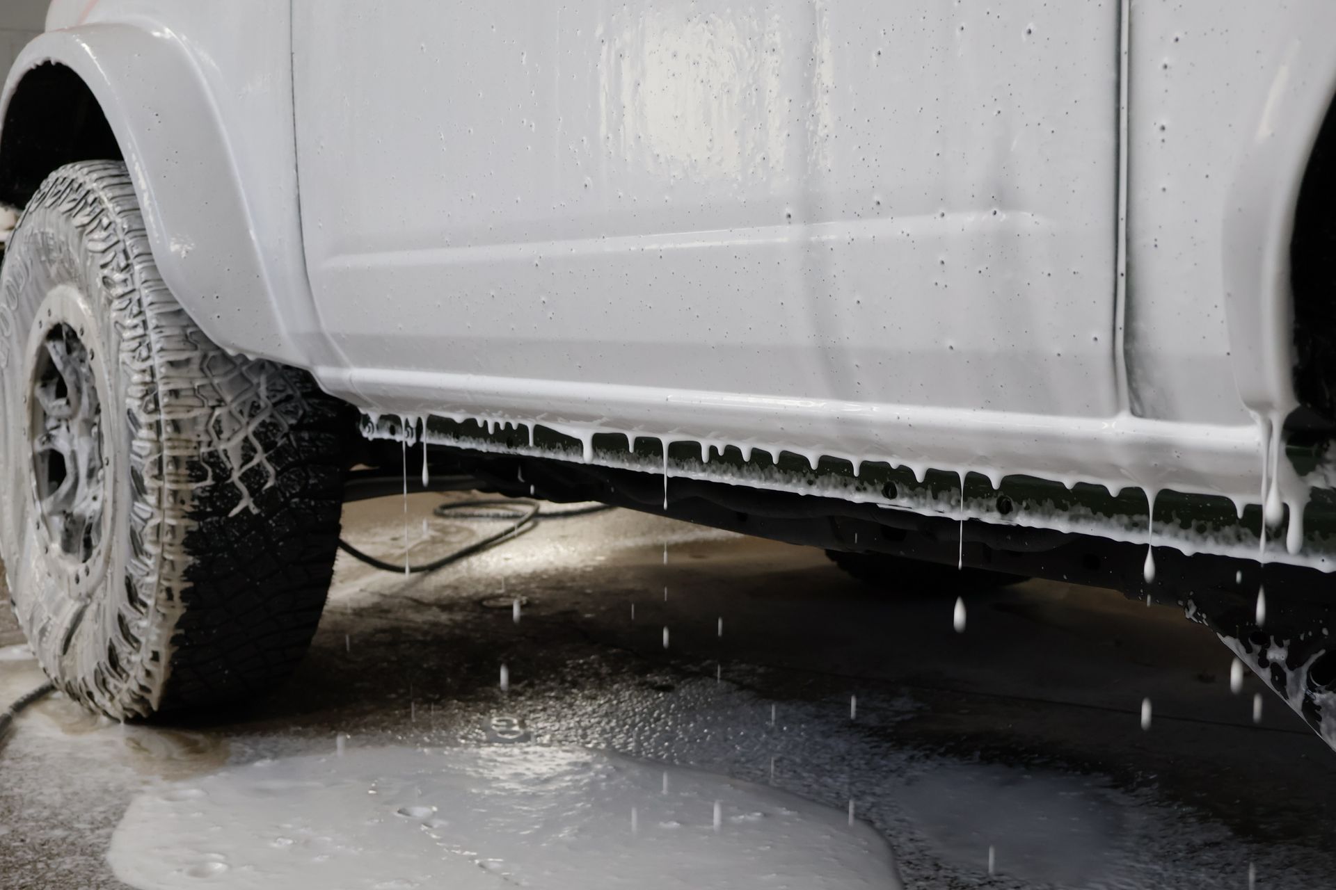 A white car covered in soapy foam, being washed. Water drips down the side.