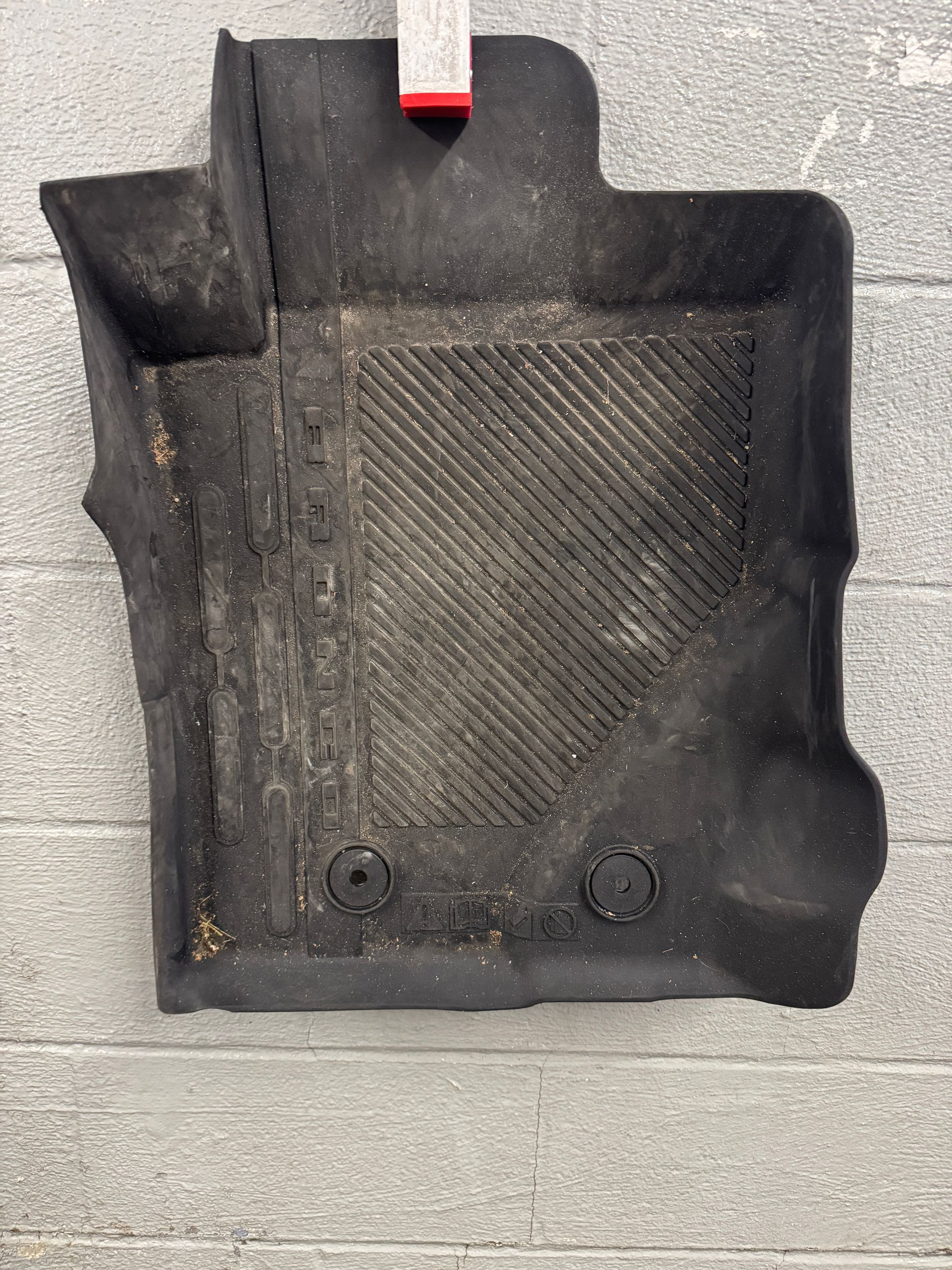 Black rubber car floor mat with dirt and wear.