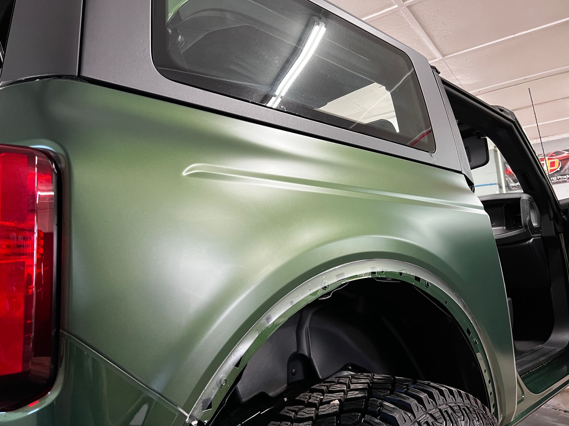 Green Ford Bronco parked on grass, black roof, near a building.