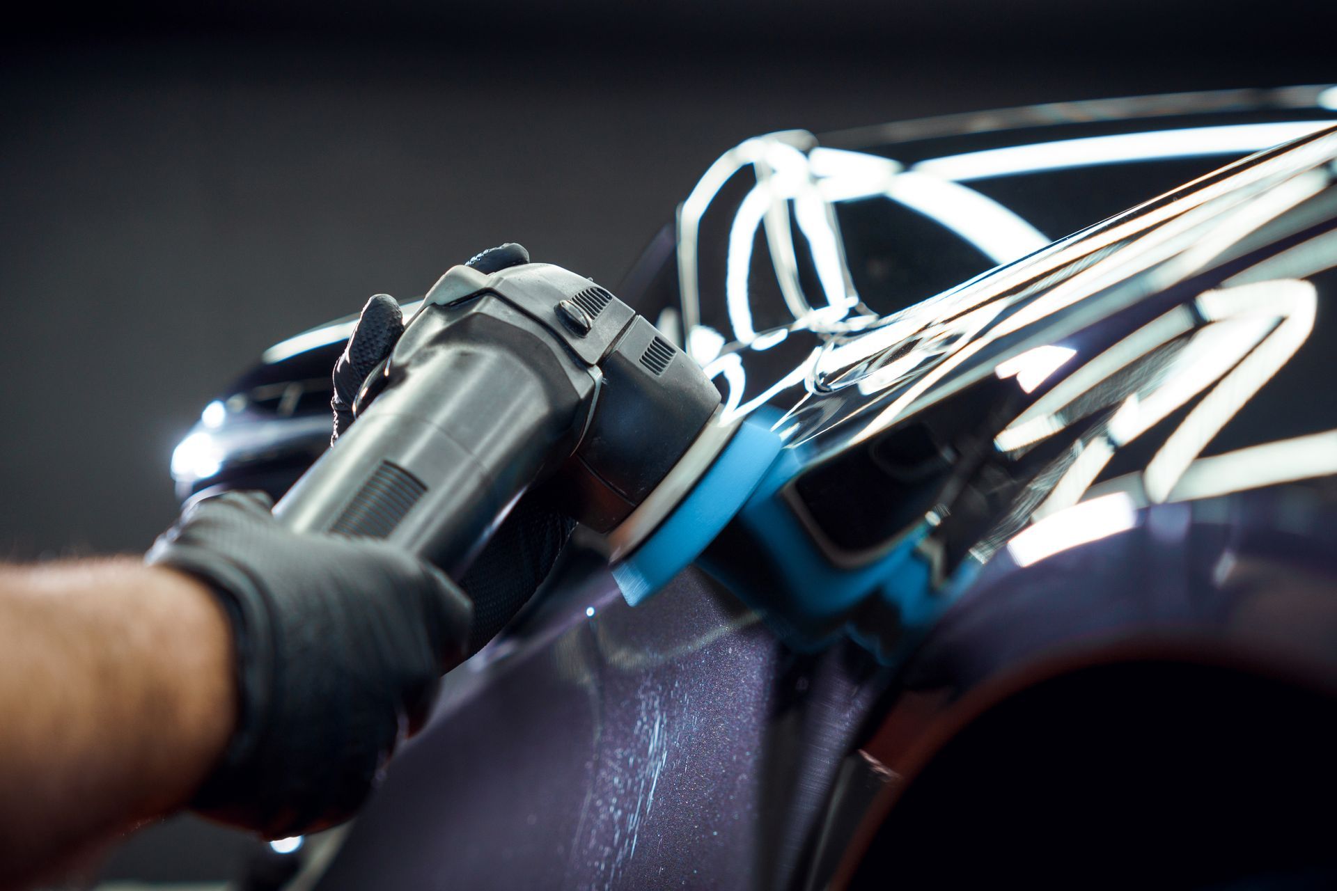 Person wearing a black glove uses a polisher on a dark car in a garage.
