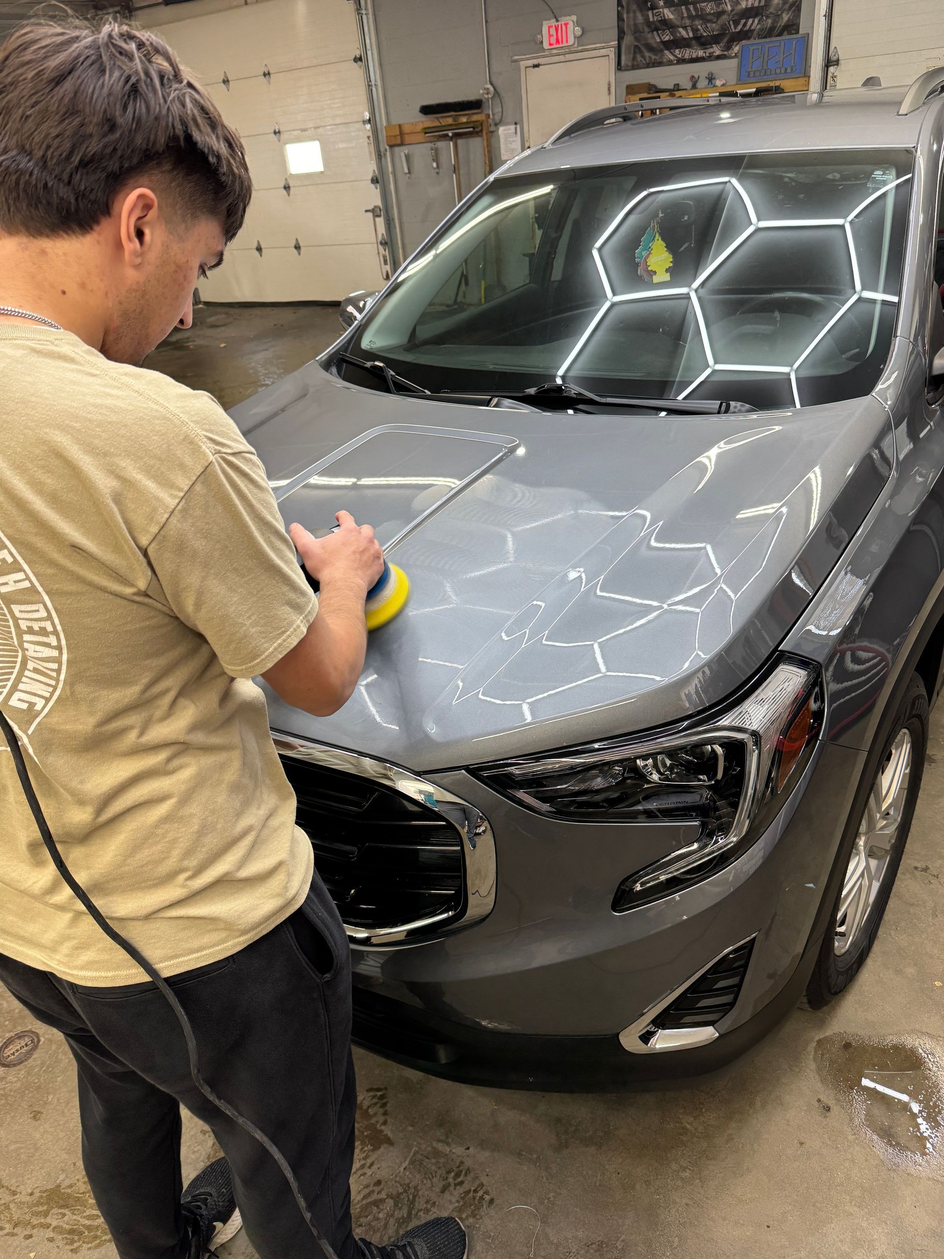 Person polishing gray car hood with electric buffer in a garage.