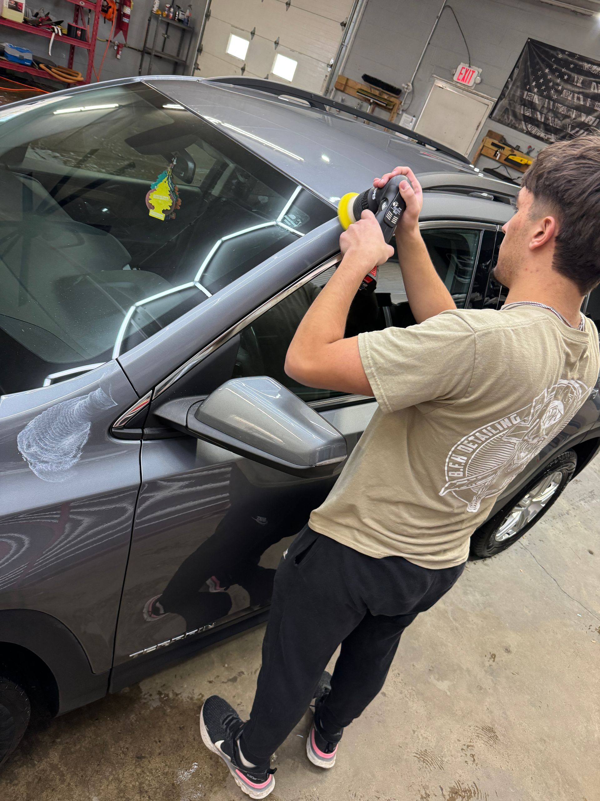 Person using a tool on a gray car in a garage.