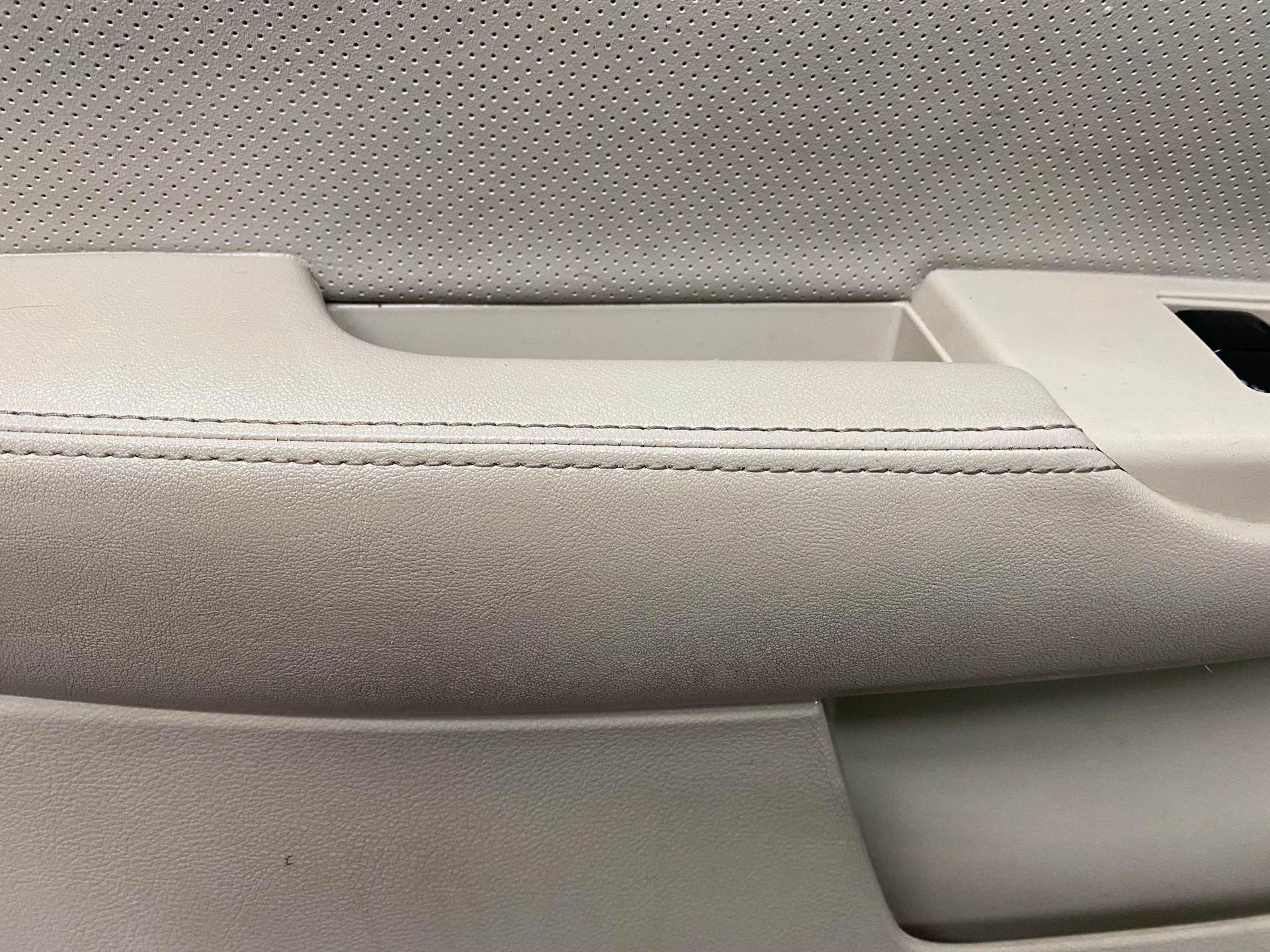Beige car door interior with textured fabric armrest and stitching detail.