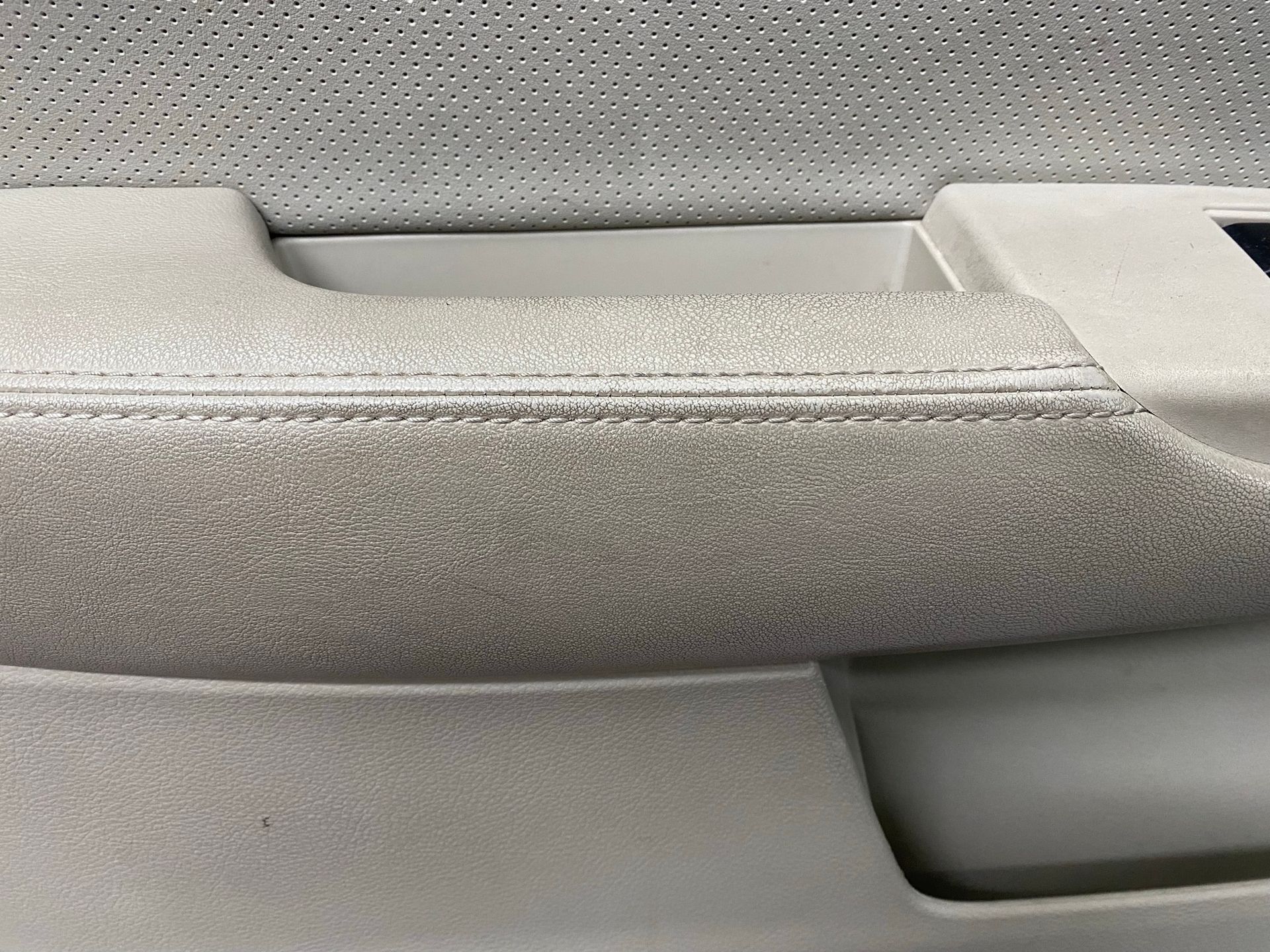 Close-up of a car's light gray suede-like door handle with stitching detail.