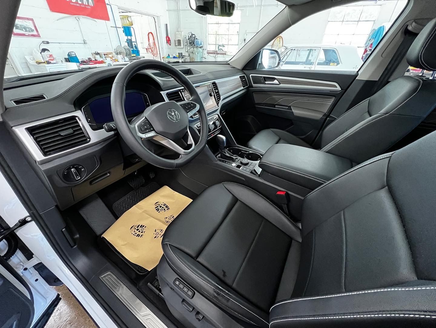 Interior view of a black leather car with steering wheel and center console. Beige floor mat.