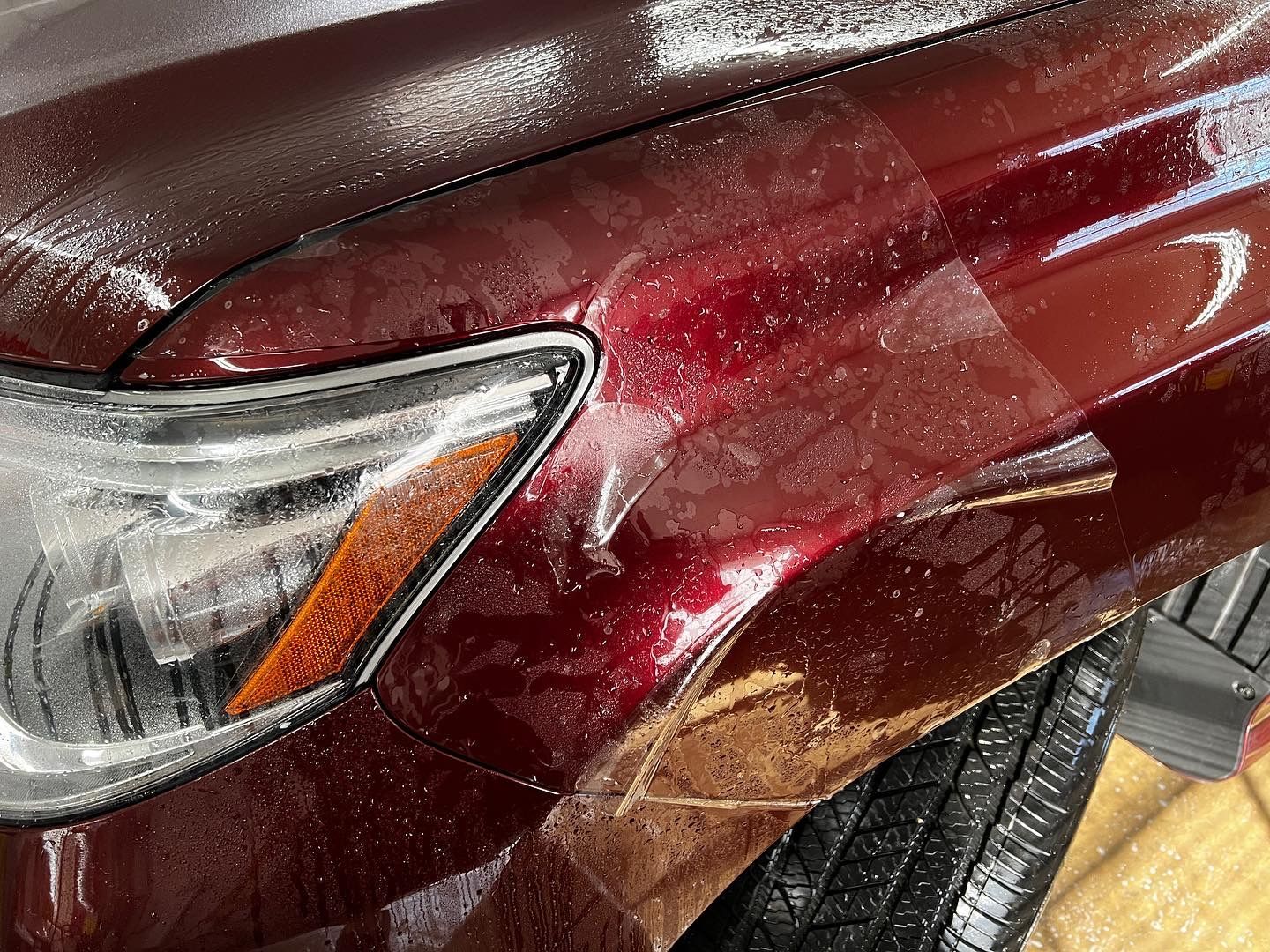 Red car fender with water droplets, headlight visible.