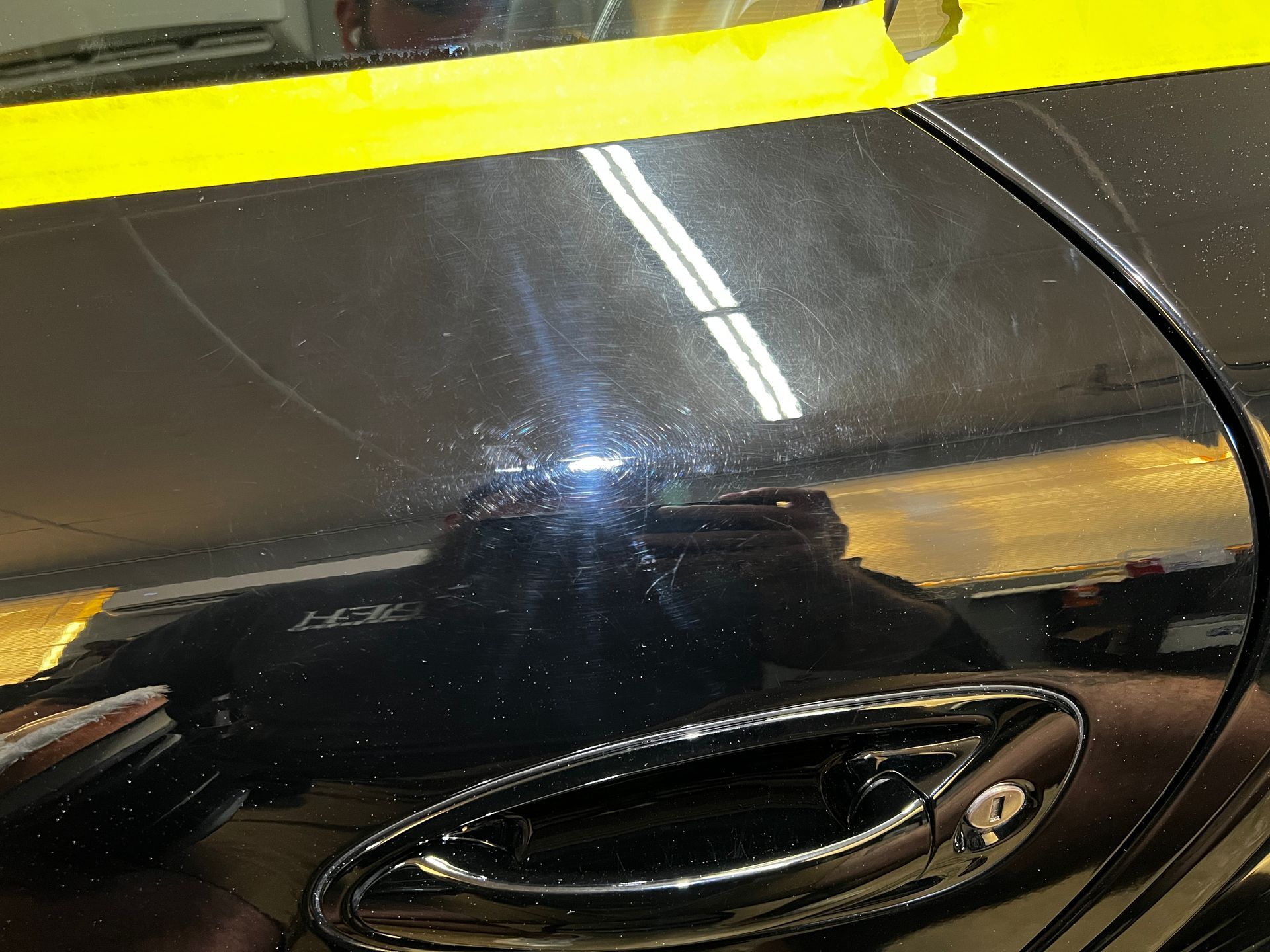 Black car door with scratches, yellow tape, and a silver handle, reflecting garage lights.