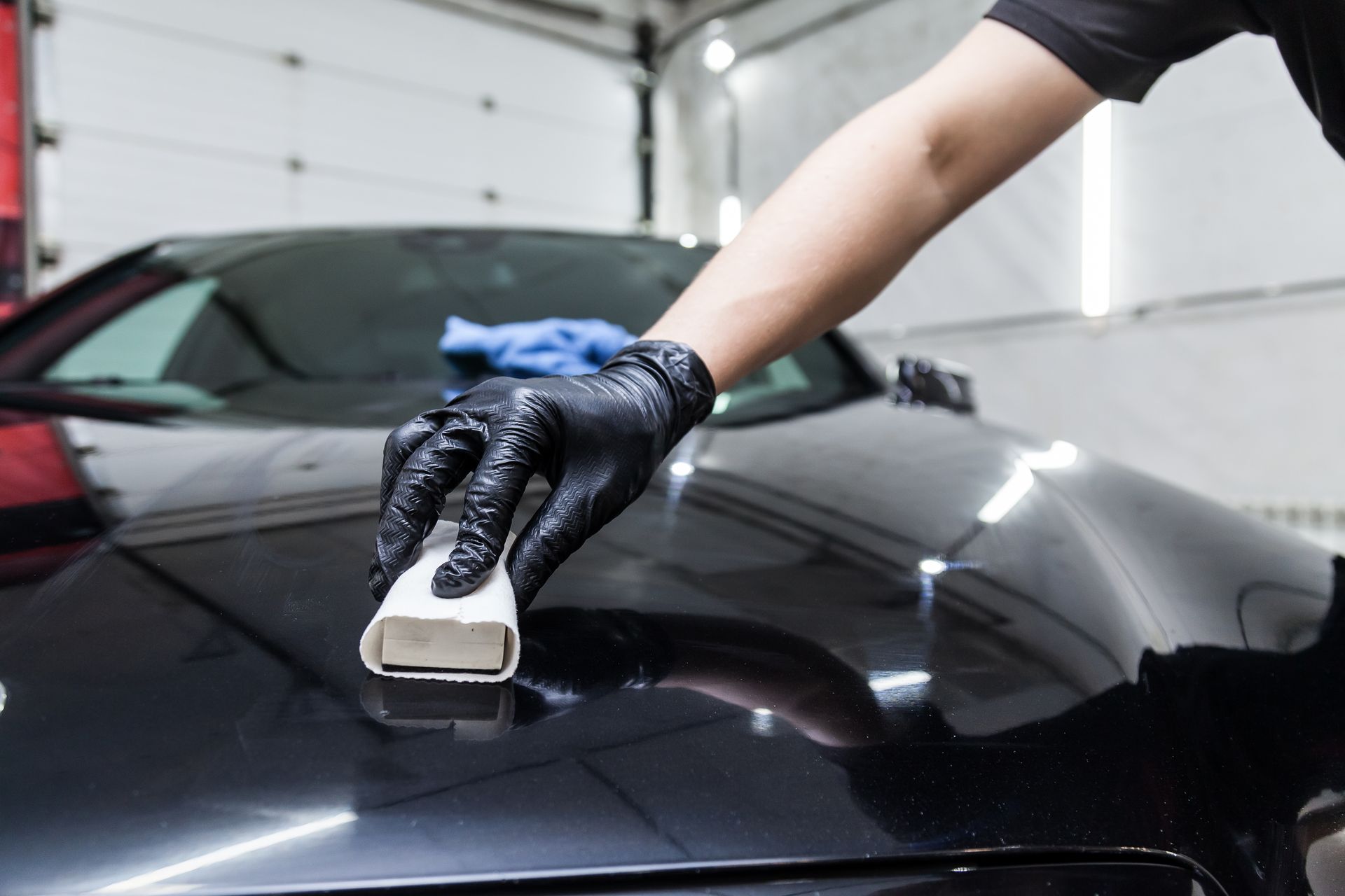 Person applying ceramic coating to a black car with a white applicator and black gloves.