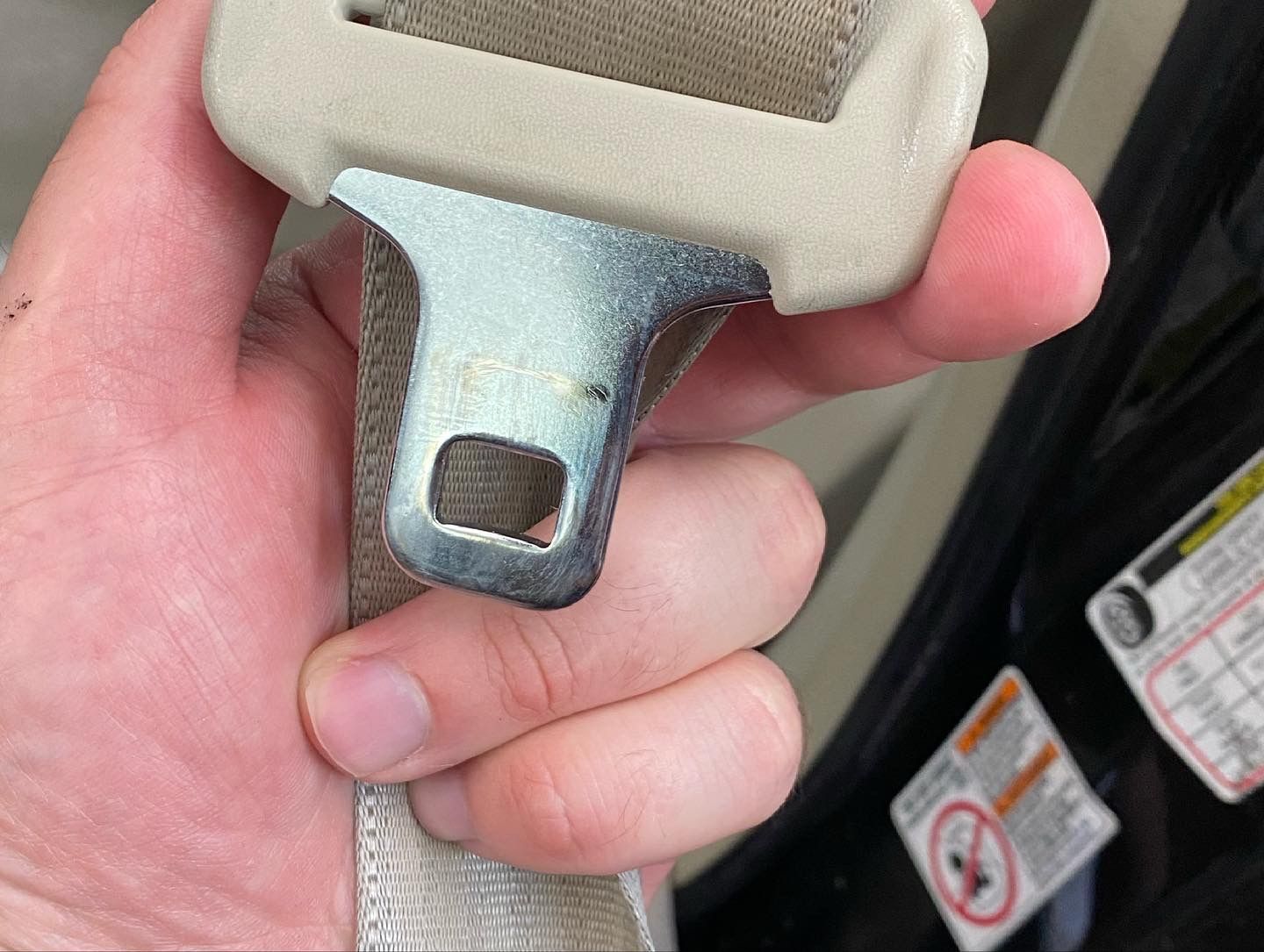 Hand holding a beige car seat belt buckle with a metal plate.
