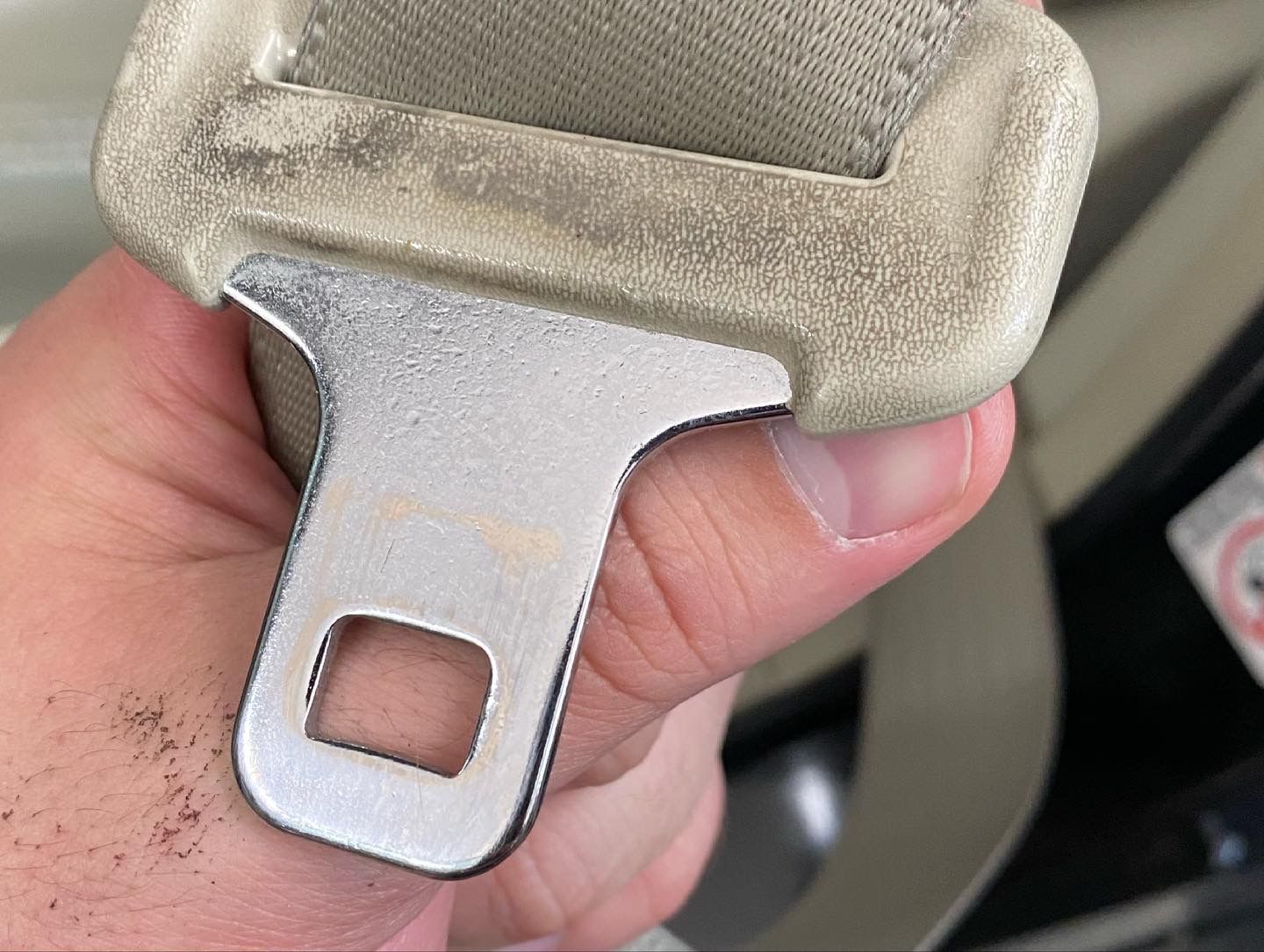 Hand holding a beige car seat belt buckle.