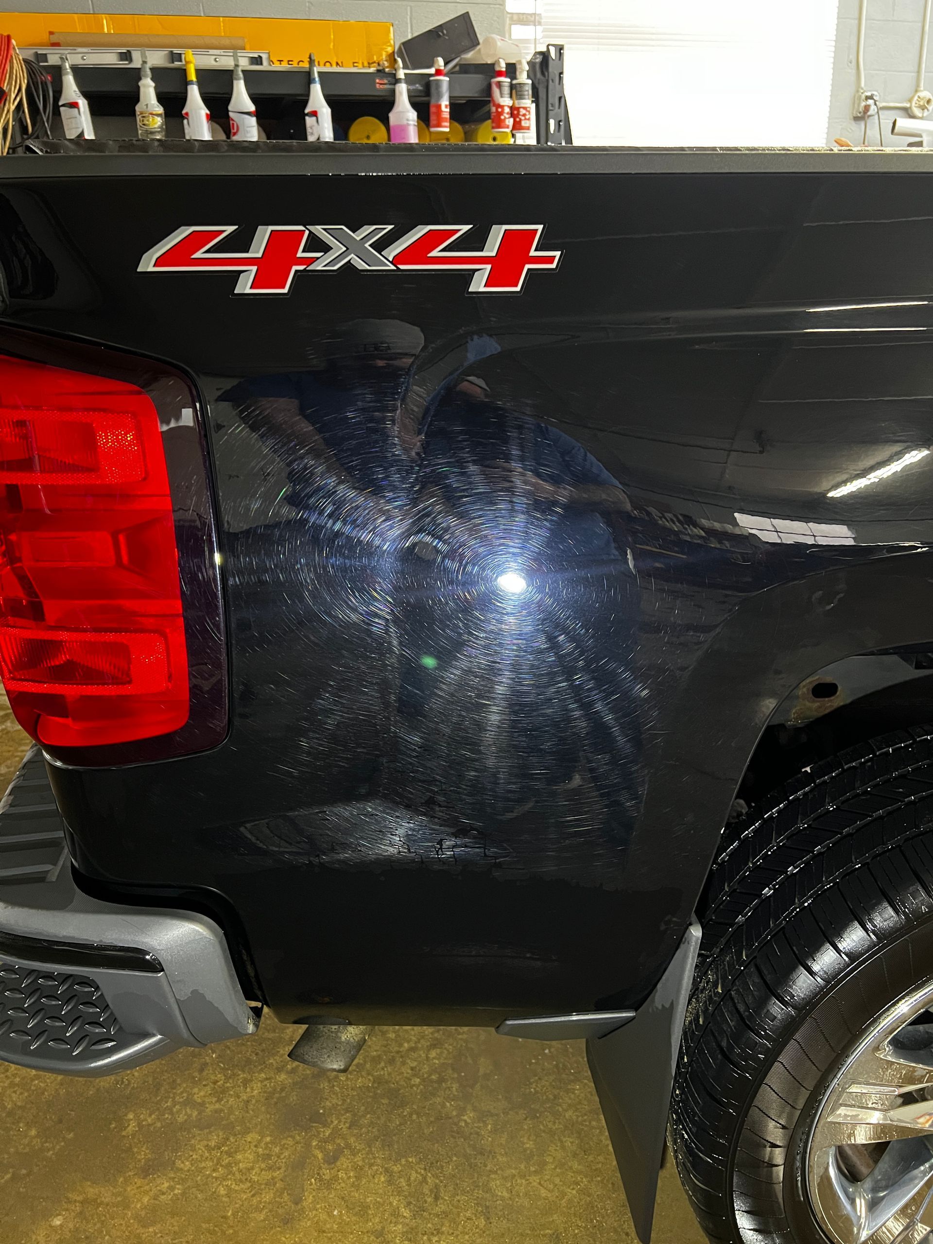 Black truck's rear quarter panel with 4X4 logo, red taillight, wet tire, and light-reflecting scratches.