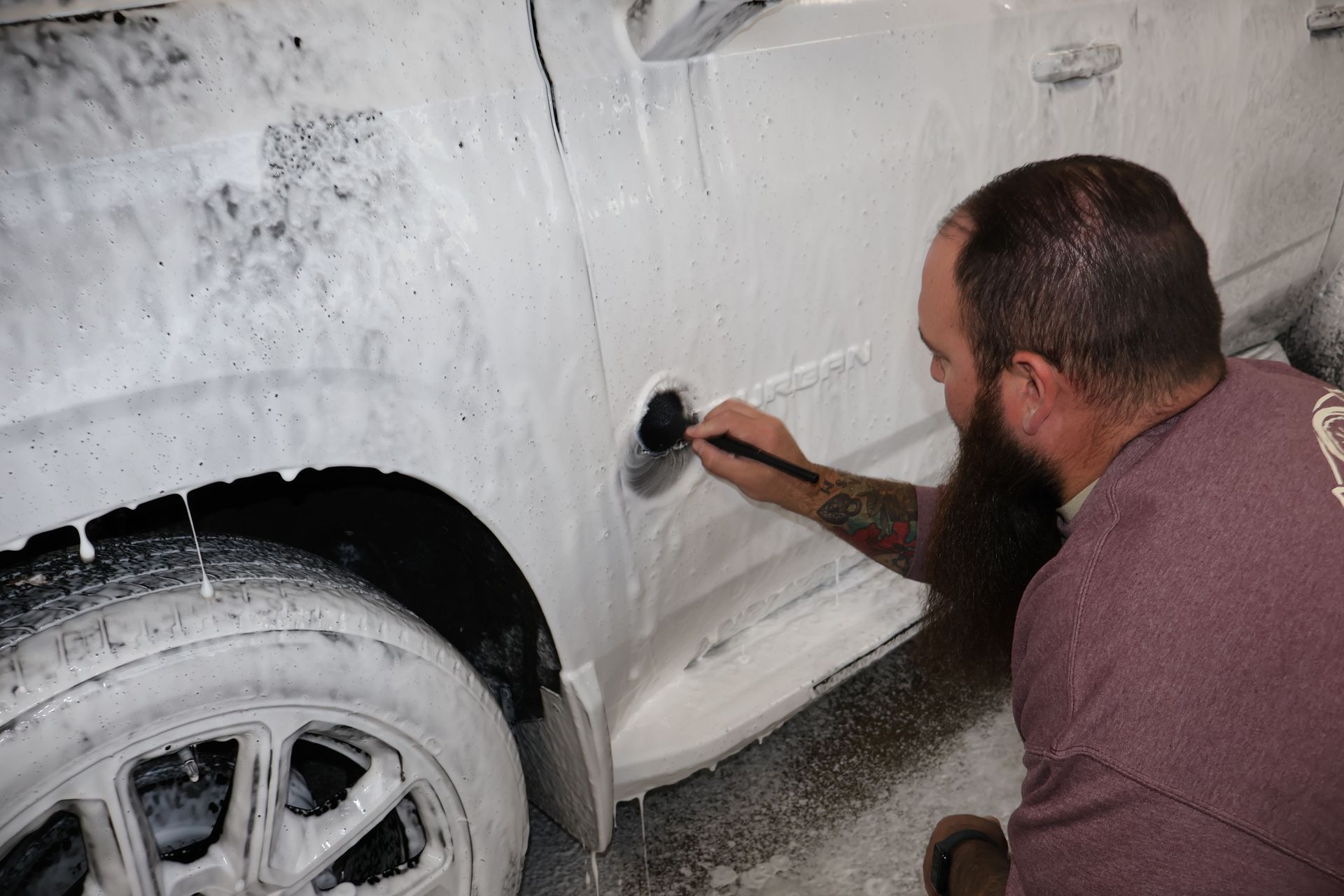 Man cleaning a car with a brush, covered in white foam.