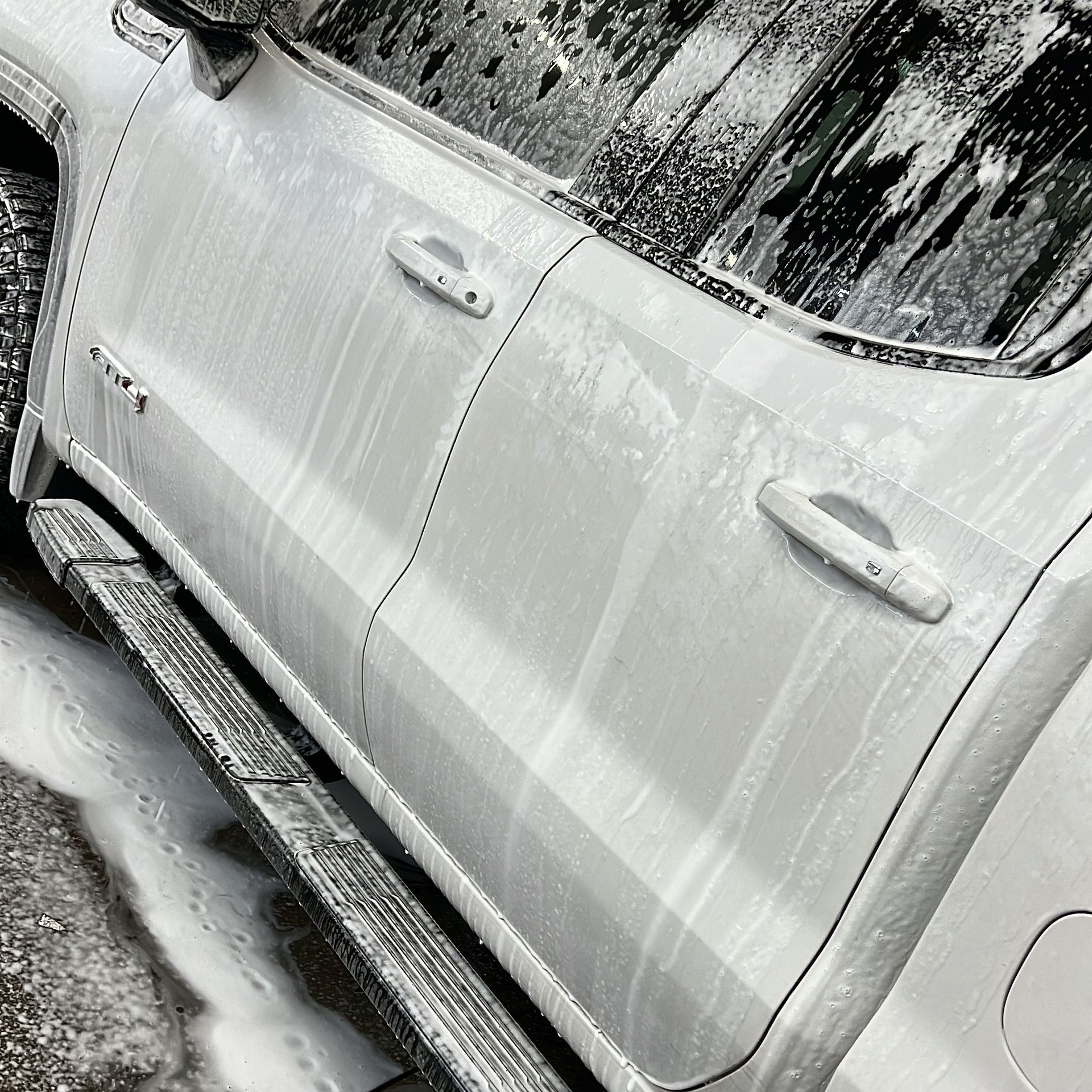 White truck covered in foamy soap suds, at a car wash.
